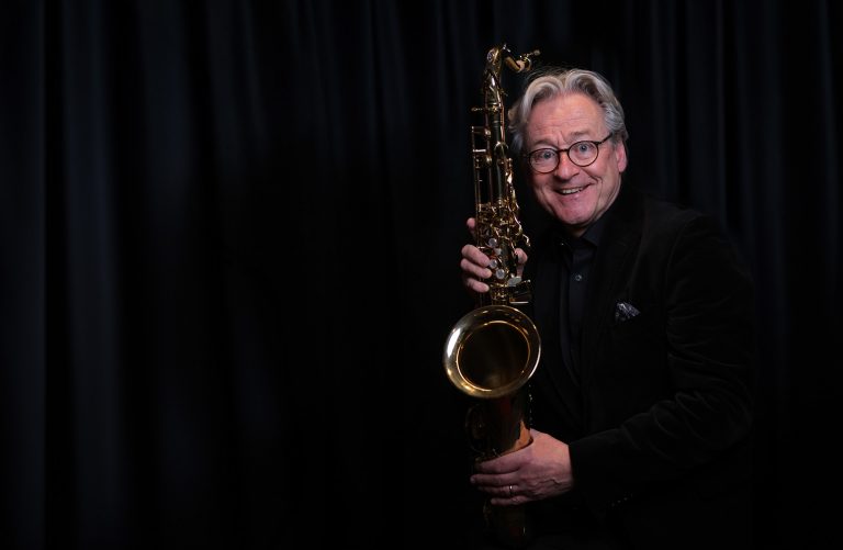 Der Musiker Jochen Hillesheim auf der Bühne am Saxophone spielen vor einem schwarzen Vorhang.