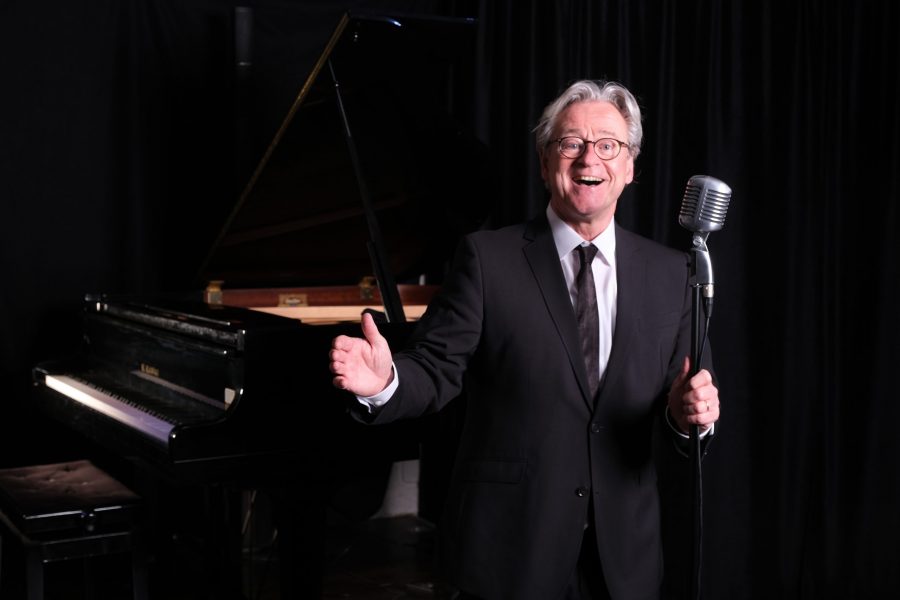 Der Musiker Jochen Hillesheim singend am Mikrofon auf einer Bühne vor einem Klavier.